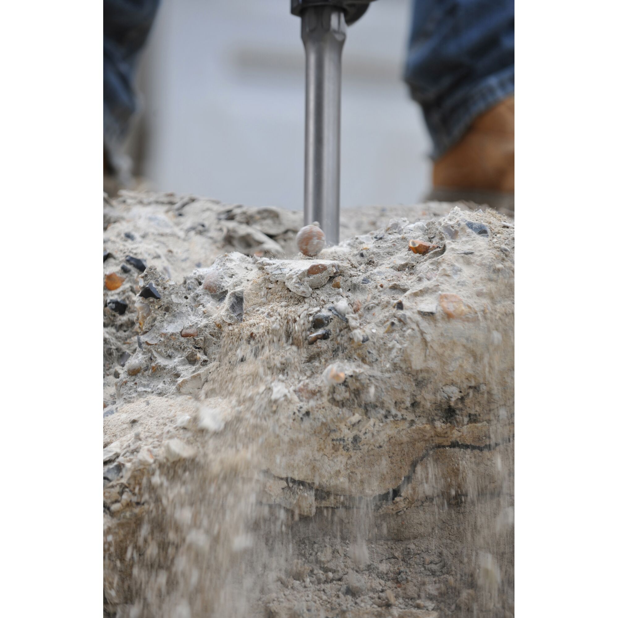 Close-up of a demolition hammer breaking concrete, with dust and debris falling as the tool is used.