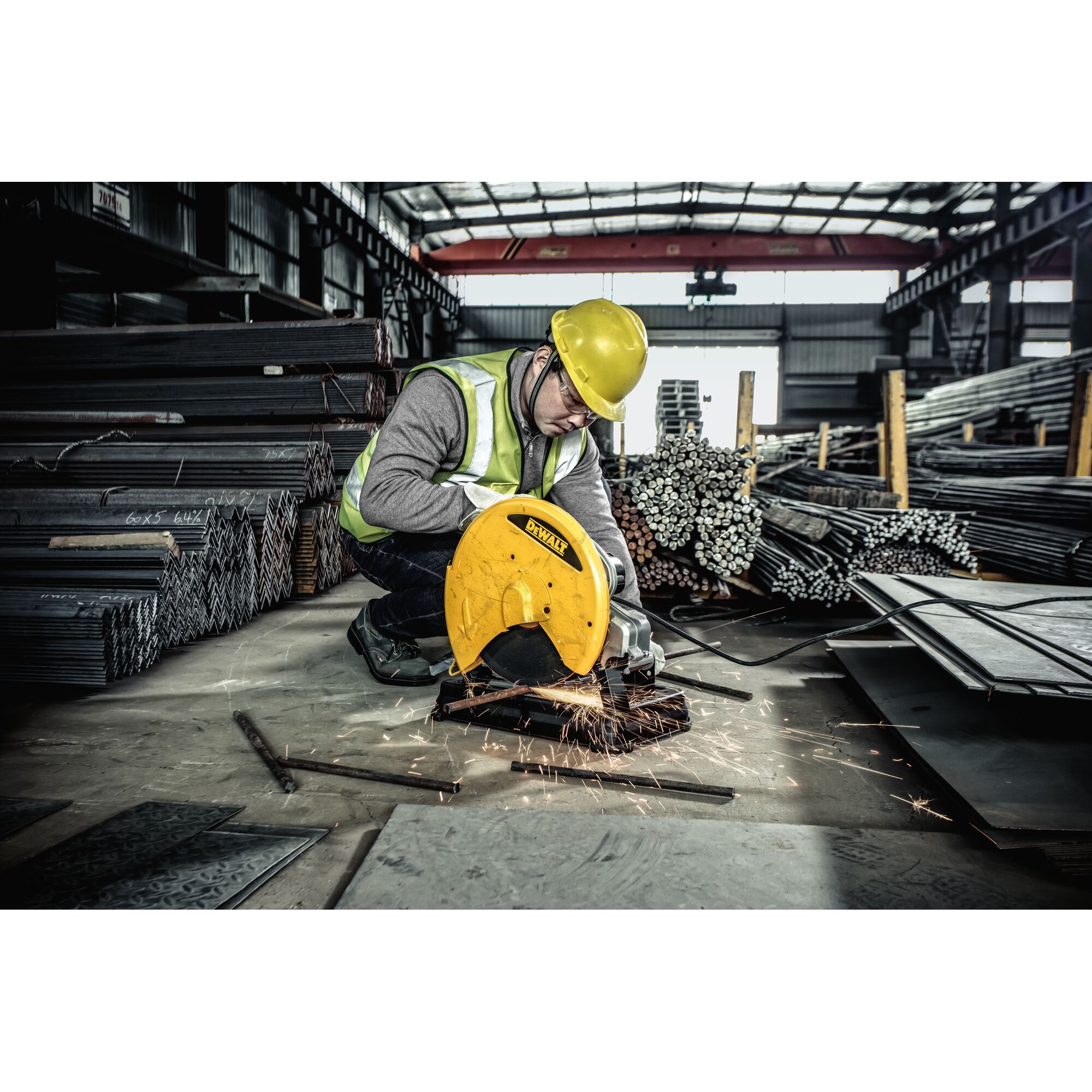 A worker wearing a reflective safety vest and yellow hard hat uses a DEWALT D28730 power tool to cut metal bars in an industrial warehouse. Sparks are visible as the tool operates, and stacks of metal materials are arranged in the background.