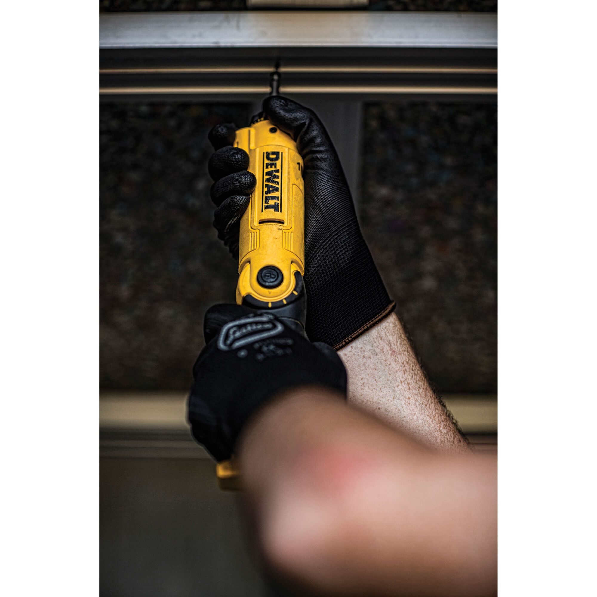 A person wearing black work gloves is using a yellow DEWALT electric screwdriver to drive a screw into a metal surface.