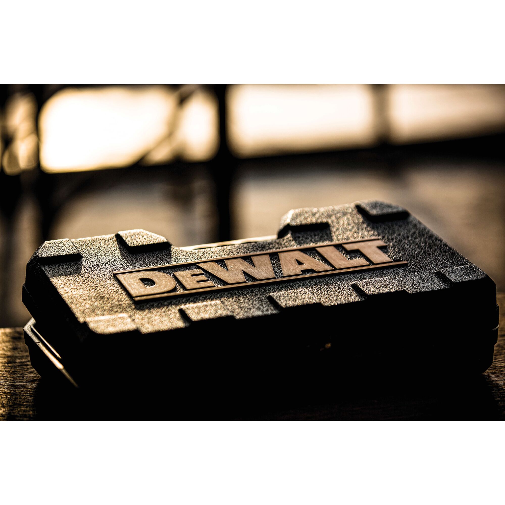 A close-up view of a rugged black DEWALT carrying case, photographed on a table with blurred background and warm lighting.