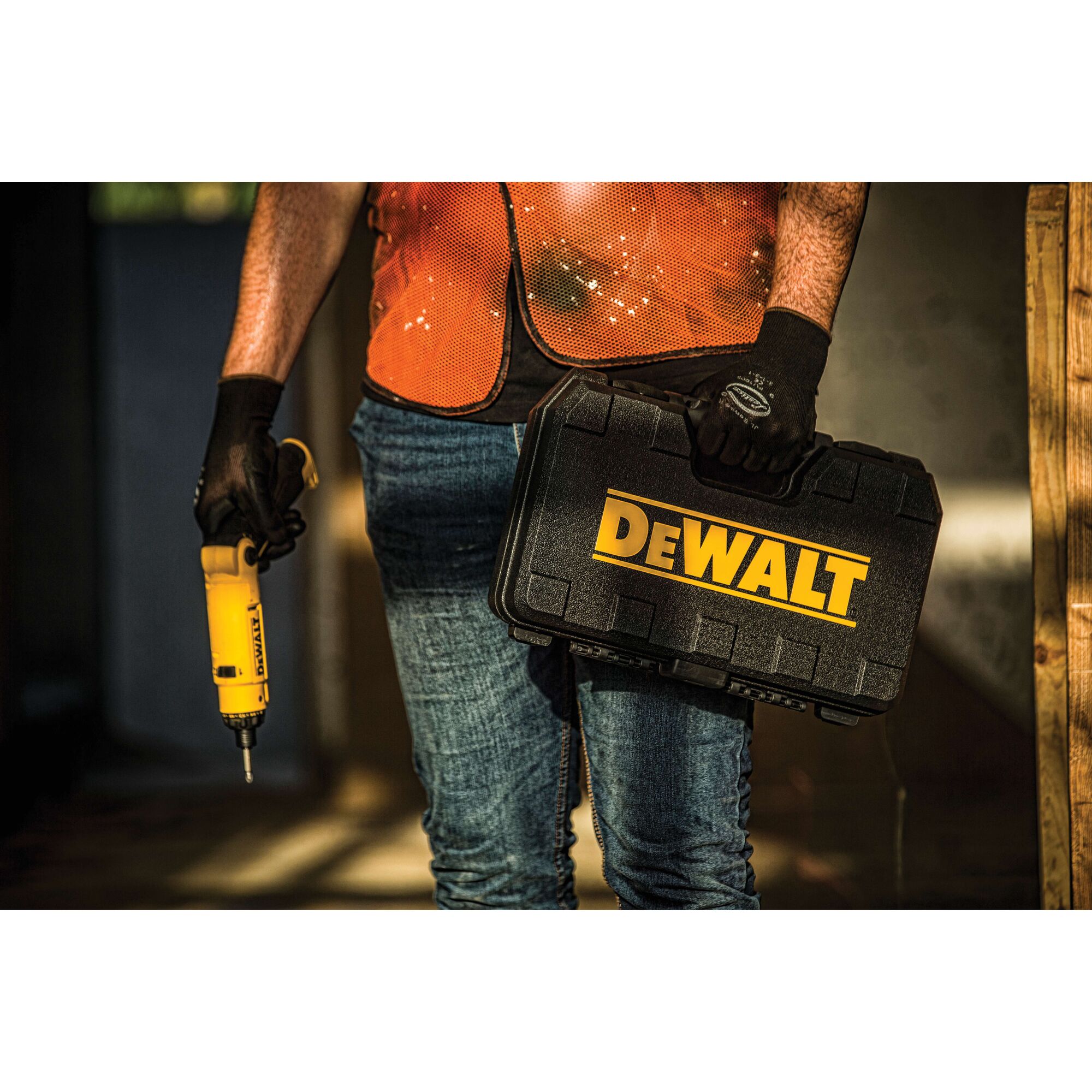 A person wearing an orange safety vest and gloves is holding a yellow DEWALT power tool in one hand and a black DEWALT carrying case in the other.