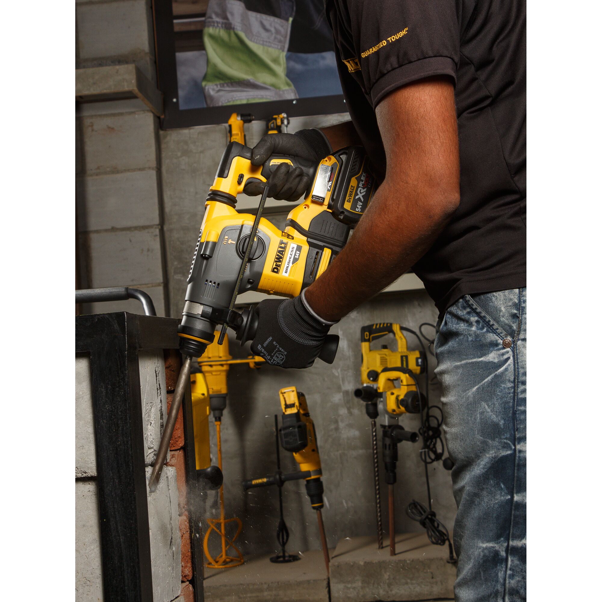 A person using a DEWALT DCH333NT rotary hammer drill to work on a concrete surface, with several other yellow DEWALT power tools visible in the background.