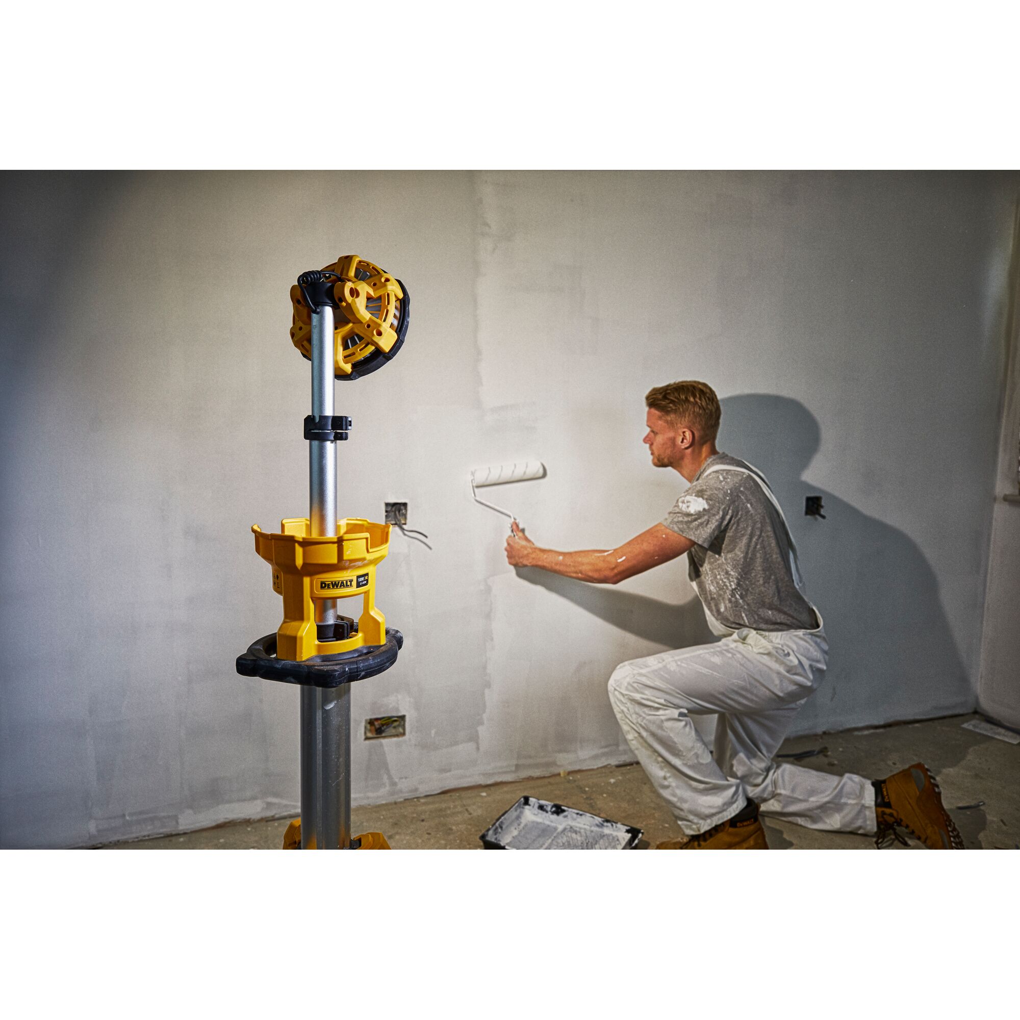 DEWALT DCL079 work light on tripod used by a painter rolling paint on a wall in a room under renovation.