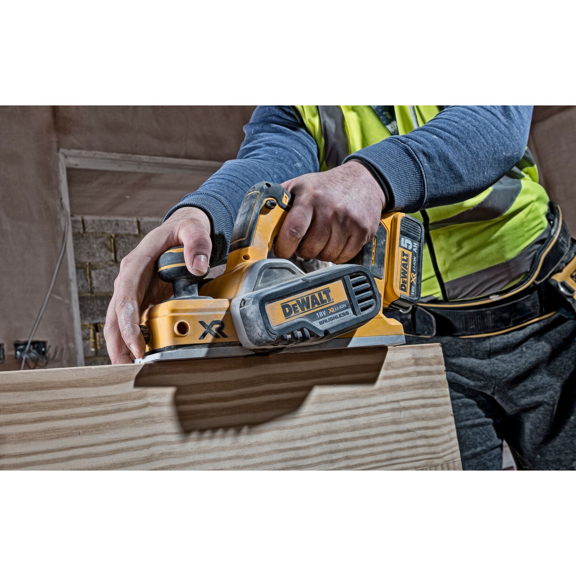 Person using a DEWALT DCP580N cordless planer on a wooden surface at a construction site.