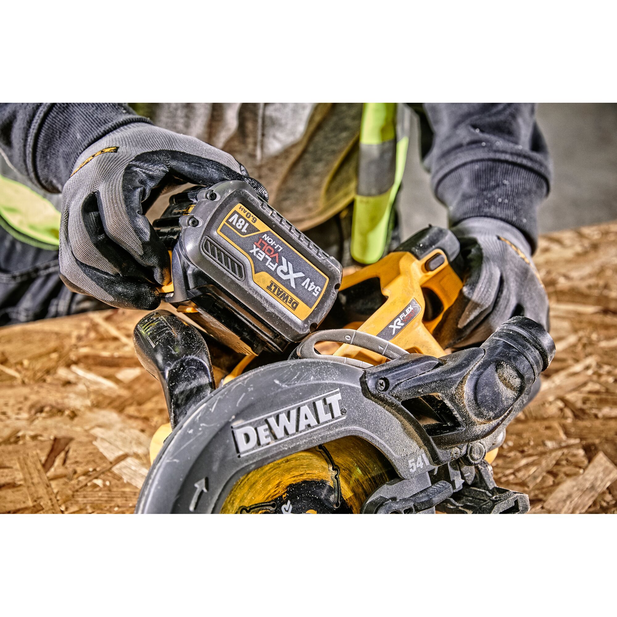 Close-up of gloved hands installing battery on a DEWALT cordless circular saw, working on a wooden surface.