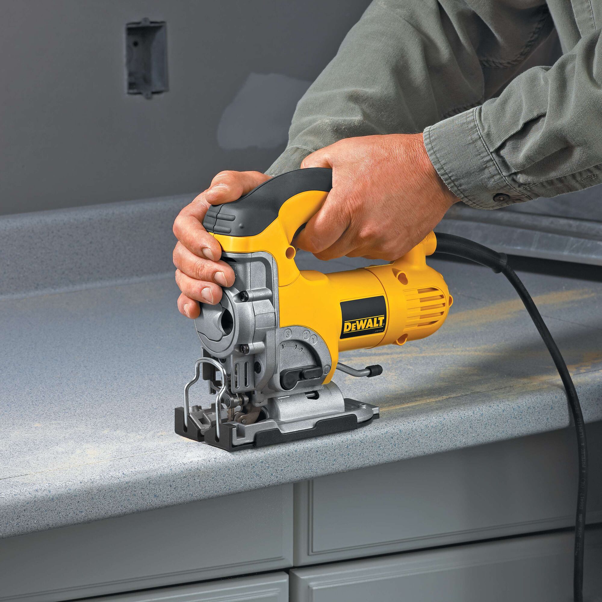 A person using a yellow and black DEWALT jigsaw to cut a countertop. The tool is plugged in and held firmly for precise cutting.