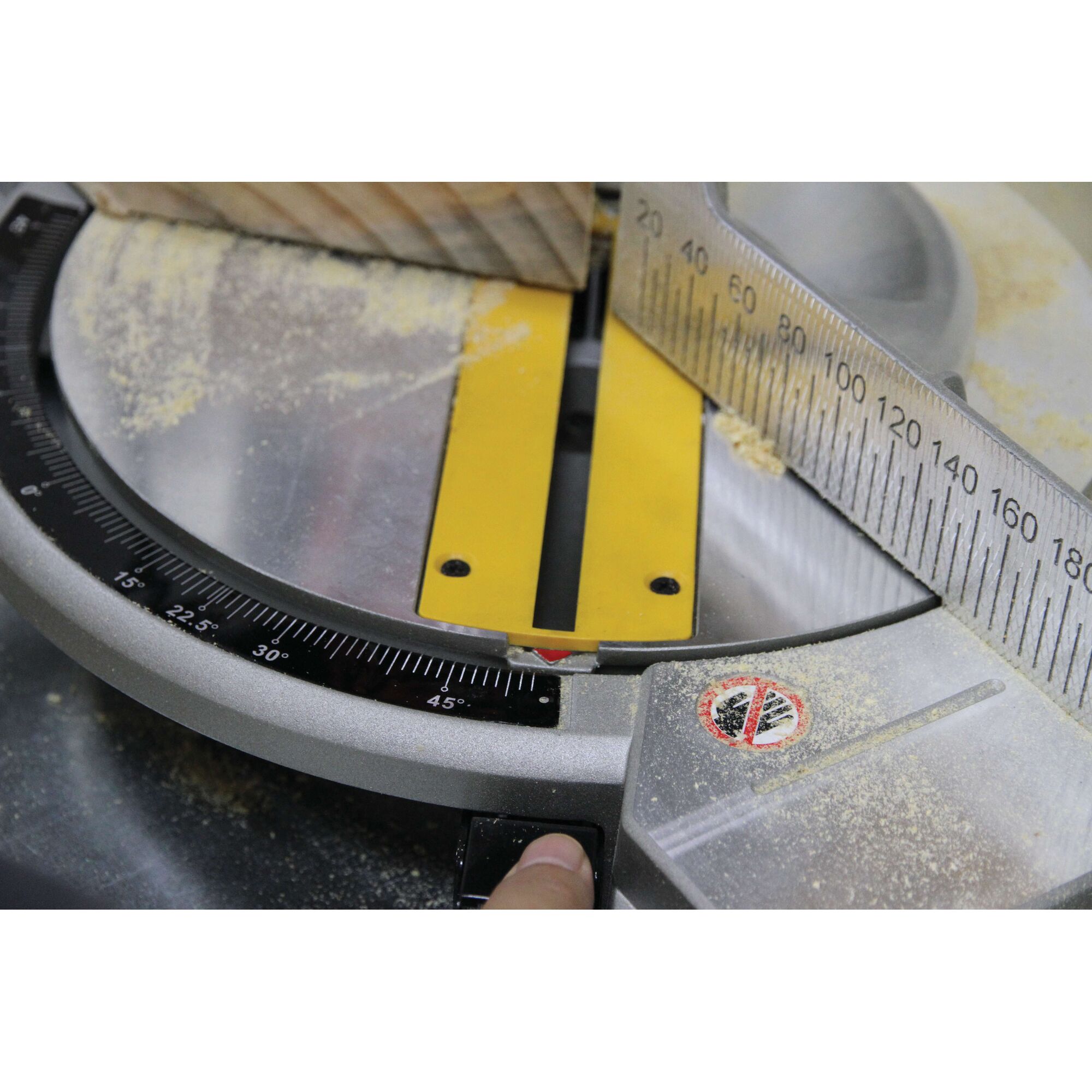 Close-up view of a DEWALT miter saw with a piece of wood placed for cutting. The saw features a measurement scale and some sawdust around the cutting area.