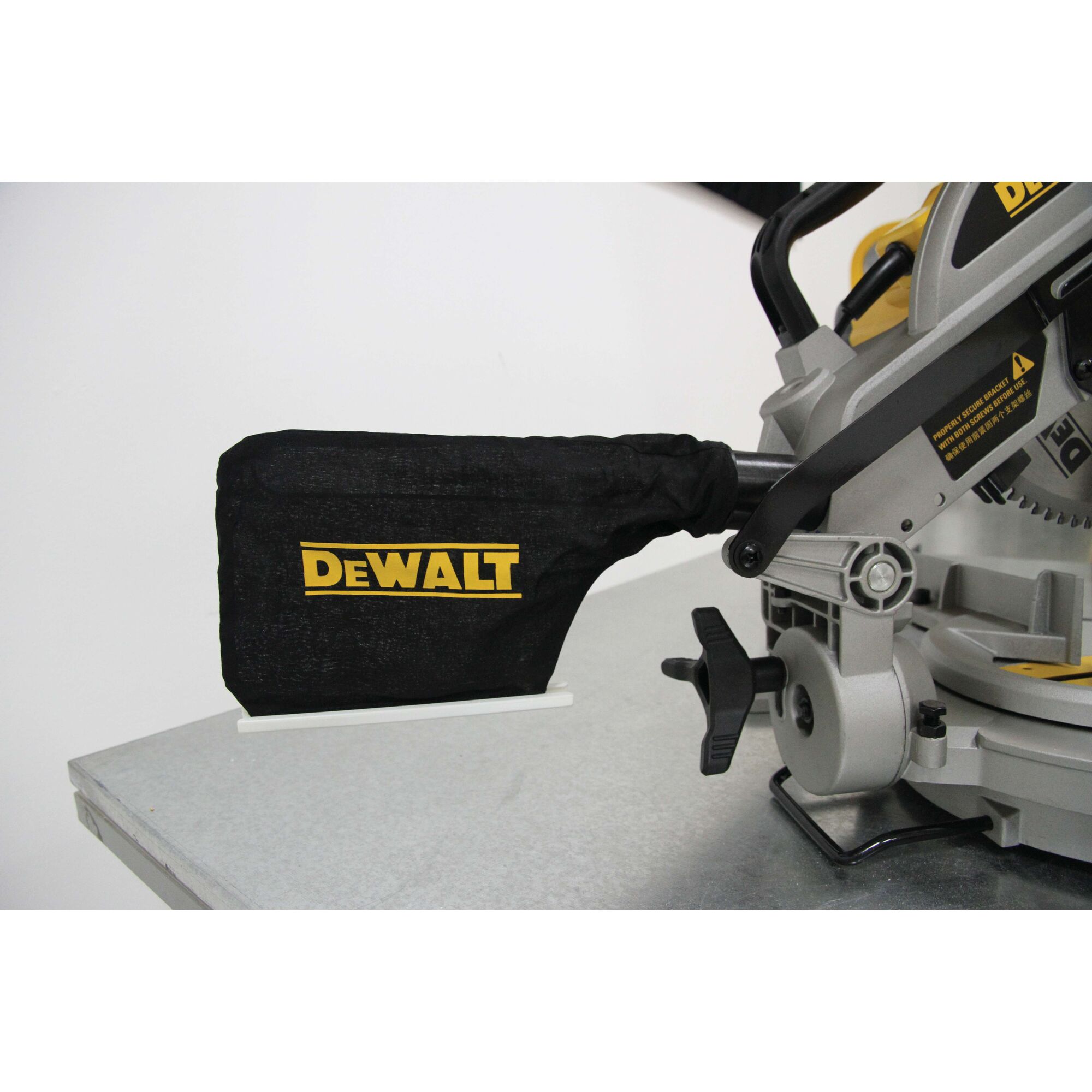 Close-up view of a DEWALT DW714 miter saw, focusing on the dust collection bag attached to the saw, placed on a metallic work surface.