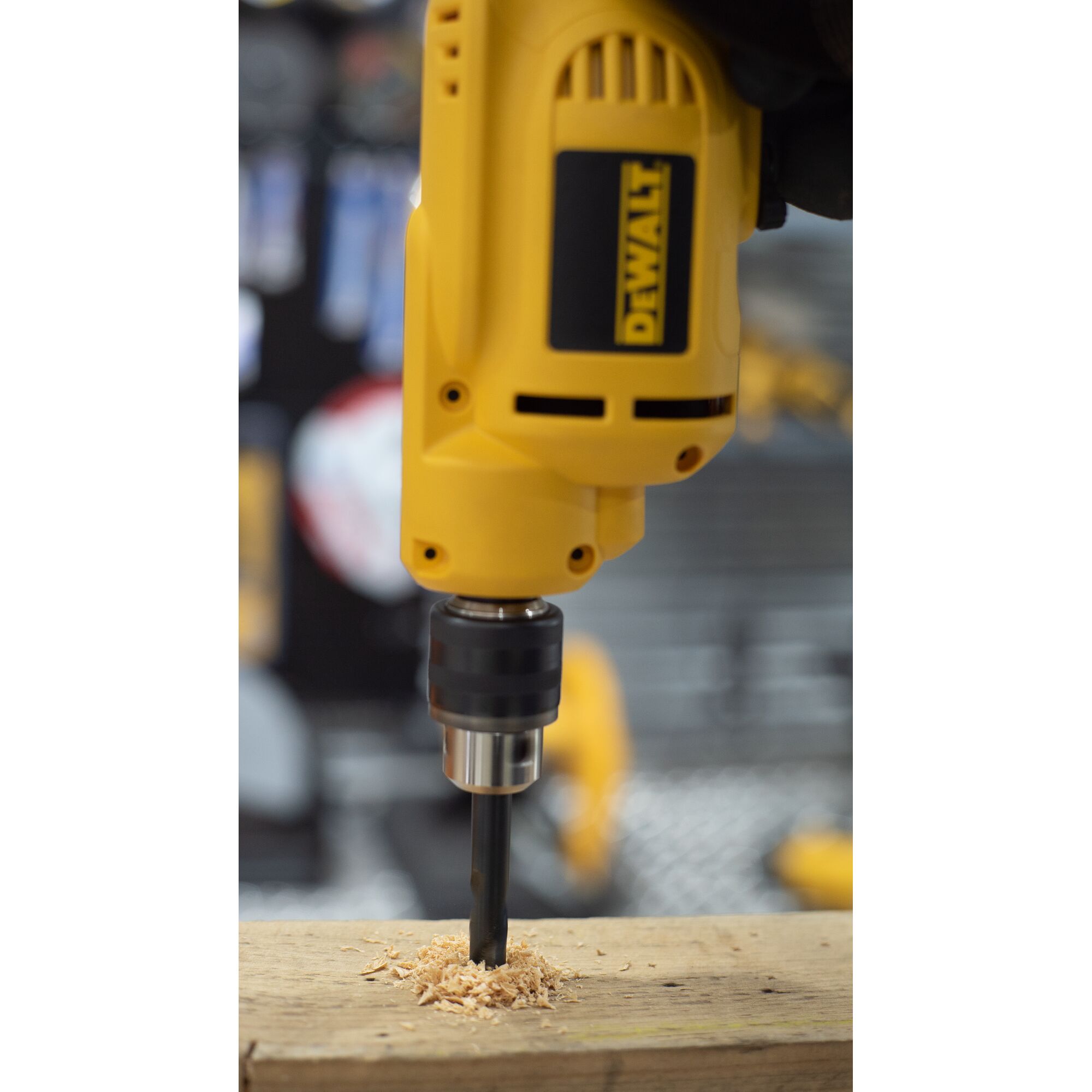 A close-up of a yellow DEWALT electric drill in use, drilling into a piece of wood with wood shavings around the drill bit.