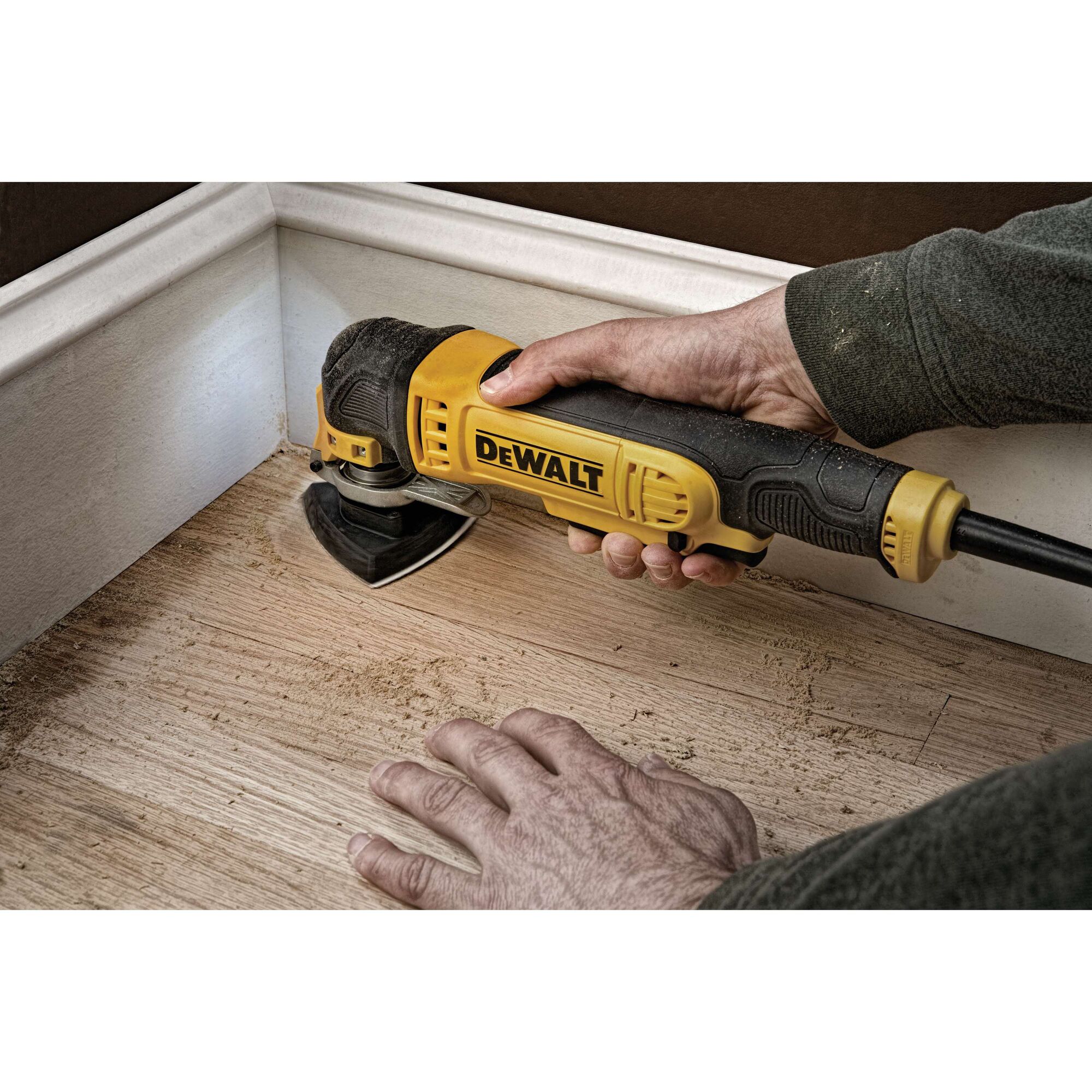 A person uses a DEWALT oscillating multi-tool to sand wooden flooring near a wall corner.