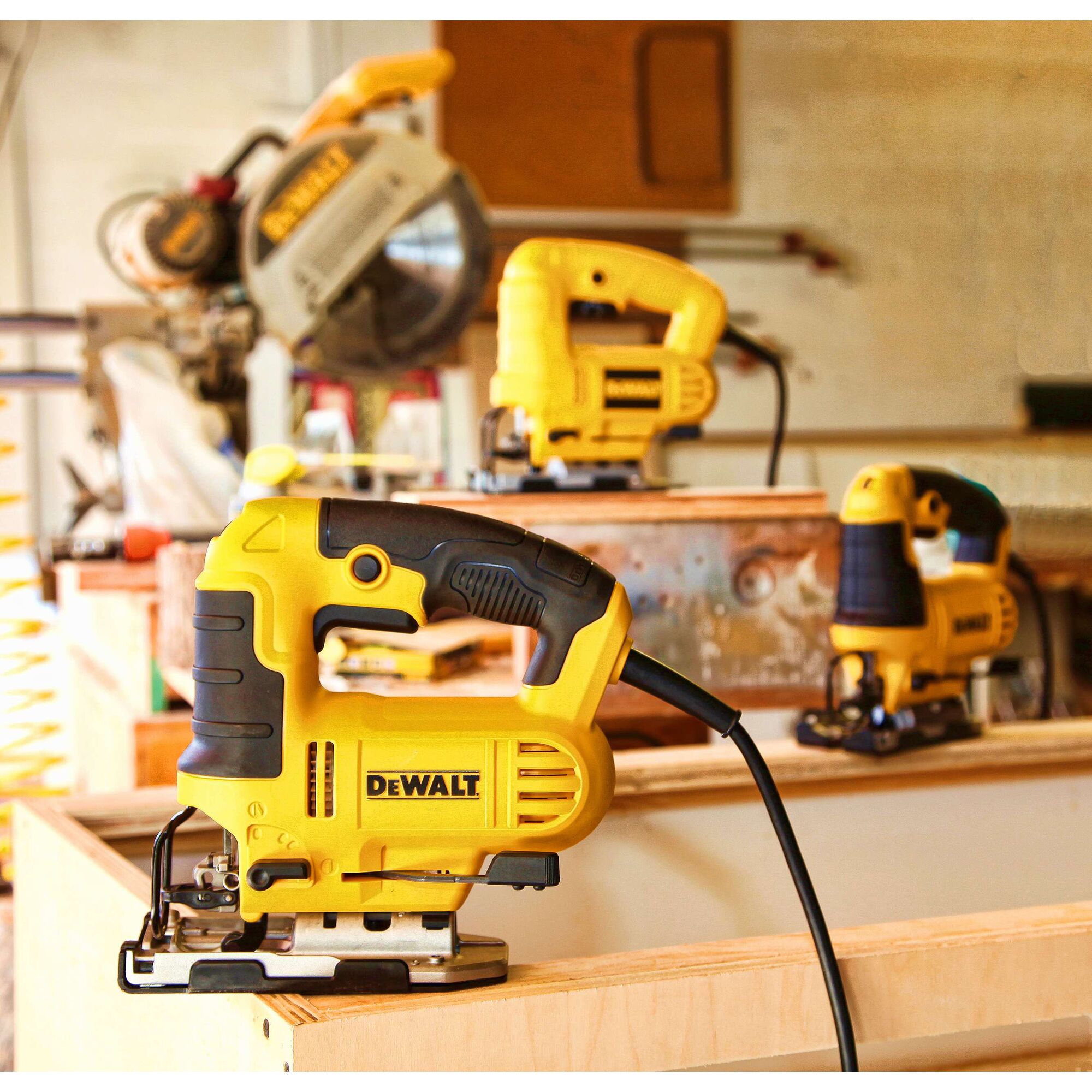 A yellow DEWALT jigsaw power tool with black accents is placed on a wooden surface in a workshop, with other similar tools and woodworking equipment visible in the background.