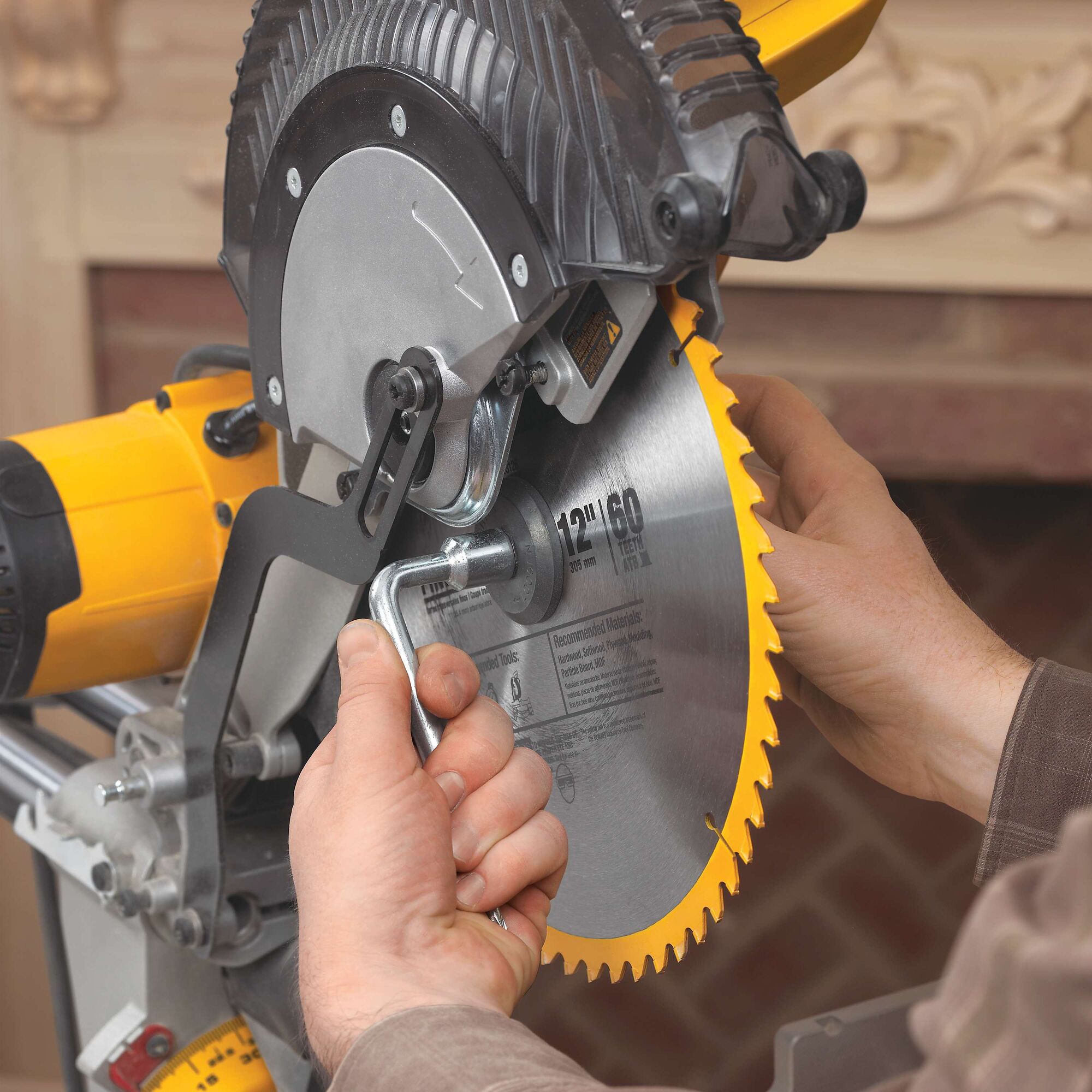 Close-up of a person changing the blade on a DEWALT miter saw, using a wrench to loosen the bolt holding the circular saw blade in place.