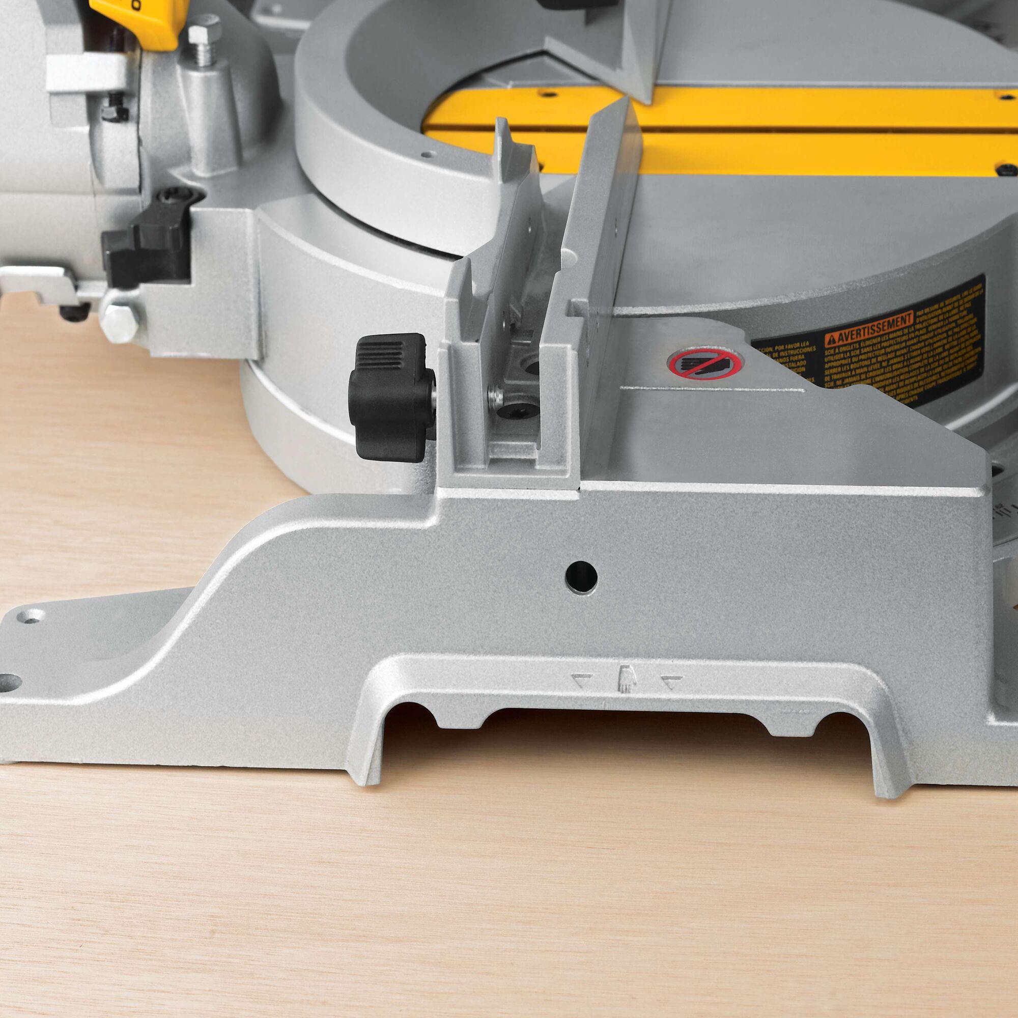 Close-up view of a DEWALT DWS780 miter saw, showing the metallic base, adjustment knob, and part of the yellow cutting guide on a light wooden surface.
